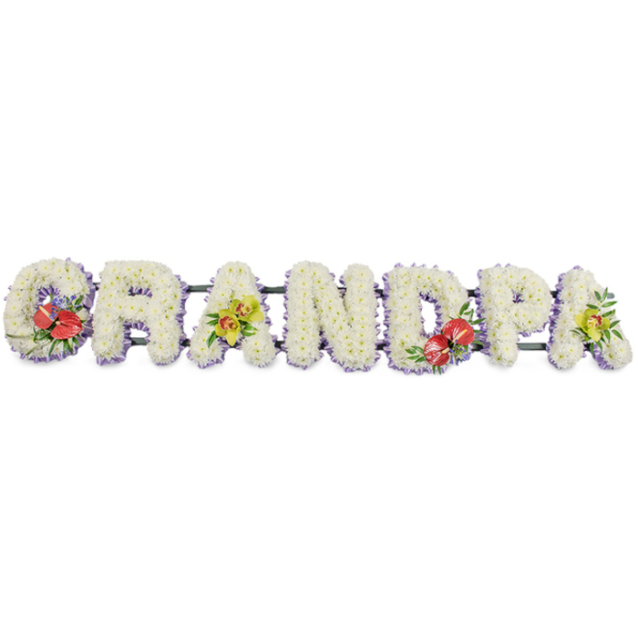 Set against a crisp white background, this bespoke sympathy arrangement spells out "GRANDPA" in imposing capital letters, the kind traditionally placed beside the coffin or on a hearse for a grandfather's funeral in the Leytonstone area. Each letter is formed from an abundance of fresh white chrysanthemums, the tiny petals layered closely together to produce a thick, cushiony surface that feels both comforting and immaculate. Around the lower edges of the letters, a soft lavender ribbon peeks through, lending a delicate border of colour that subtly outlines the word without overpowering its serene whiteness. The letters are mounted on slim dark green bars, barely visible beneath the flowers yet essential for holding the tribute steady when displayed at a local chapel or crematorium near Wanstead or along the High Road. To break the expanse of white and add personal character, the florist has placed four distinct sprays. On the "G" and the "D," eye-catching clusters of deep red anthuriums with characteristic heart-shaped, glossy petals and strong central spadices are arranged among lush green foliage, the rich crimson tones symbolising deep affection and cherished memories. On the first "A" and the last "A," delicate yellow-green orchids provide a lighter, more tranquil note, their sculpted petals and intricate throats casting subtle shadows that hint at sophistication and enduring beauty. The tribute as a whole feels carefully considered and lovingly crafted, the sort of custom funeral flowers families in Leytonstone might choose to honour a gentle, much-admired grandparent whose presence shaped everyday life close to local parks, schools, and familiar streets.