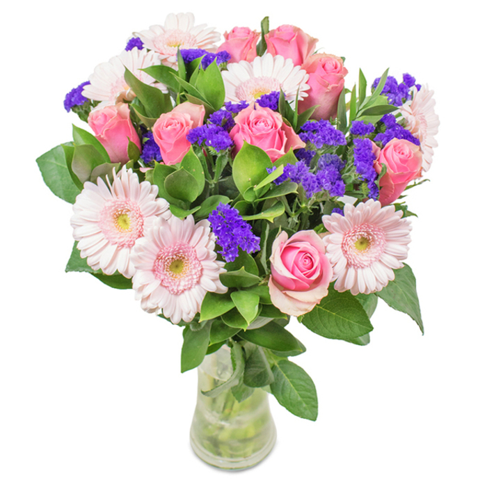 Presented in a clear glass vase against a crisp white backdrop, this floral arrangement features approximately 7-9 soft to medium pink roses, their petals elegantly shaped in classic spirals-some just beginning to unfurl, others still tightly closed-exuding the promise of their full bloom. About 5-7 pale pink Gerbera daisies, each with large, radiant heads and nearly white centers, accompany the roses, their form inviting the eye to linger over each petal. Interspersed throughout are vivid purple statice, lending both textural interest and pops of deeper colour. Lush, deep green foliage weaves between the blooms, bringing abundant freshness and evoking the leafy calm of Leytonstone's George Green. The clear vase displays pristine stems and water, underscoring the natural elegance and freshness of a same-day flower delivery from the neighbourhood's local shops. This arrangement, with its harmonious blend of pinks and purples, suits celebrations from birthdays to anniversaries, Mother's Day, or as a refined accent for a High Road office-conveying joy, affection, and a touch of Leytonstone's vibrant character in every glance.